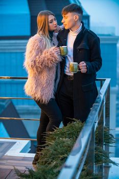 couple with mugs on the terrace of a high-rise building and look at the opening view