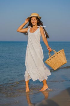 woman in a hat and with a basket in her hands is walking on the beach