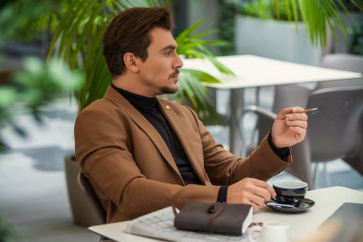 a man in a business suit sits at a table and smokes