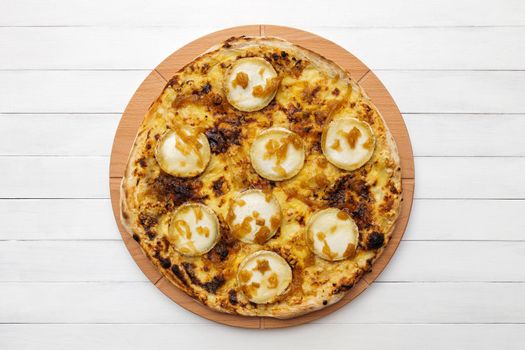 Whole round pizza topped with goat cheese and caramelized onion on wooden plate. Top view on white board background. Copy space.