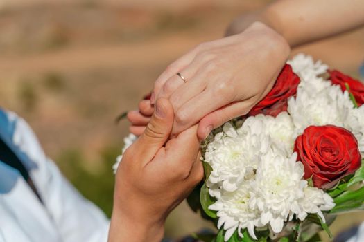 Hands of the groom and the bride with wedding rings on top of the bride's bouquet