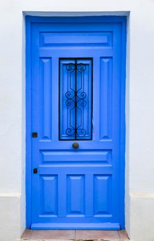 Blue wooden door with black metal knocker and whitewashed facade in Altea, Alicante, Spain.
