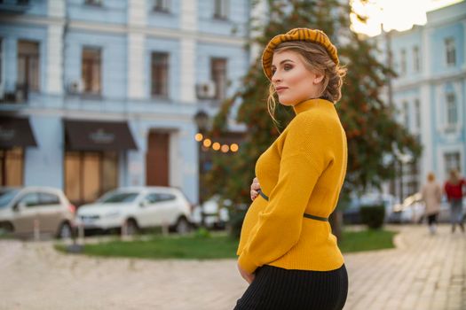 pregnant woman in a yellow sweater on the background of the city