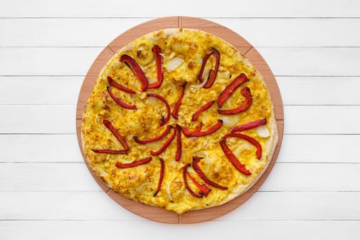 Whole round pizza topped with red pepper, onion and yellow curry sauce on wooden plate. Top view on white board background with copy space.