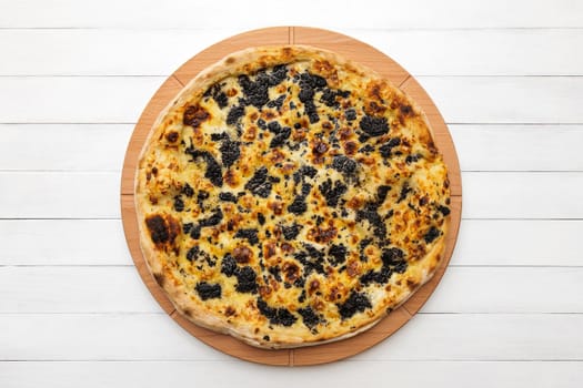 Whole round pizza topped with truffles and cheese on wooden plate. Top view on white board background. Copy space.