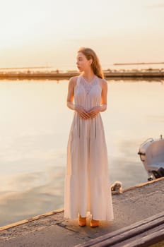 a girl in a white dress stands on the pier against the background of the sea