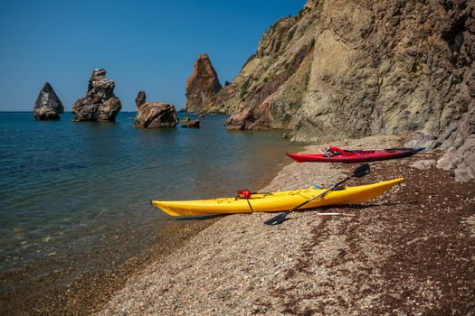 Two kayaks yellow and red on the shore of a small shingle wild beach against the background of rocks in the sea, Fiolent, Crimea.