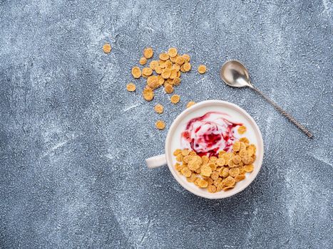 greek yogurt with jam and muesli in white bowl on grey blue concrete stone table, top view, copy space.