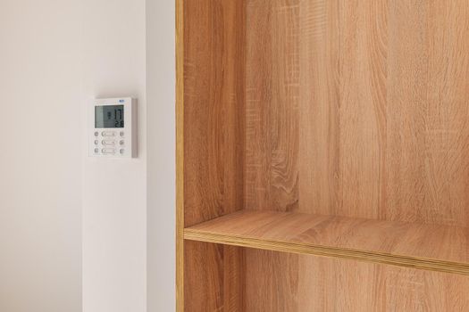Climate control panel on the wall in a room with wooden built-in furniture with shelves.