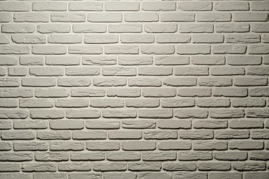 White brick wall of a warm shade lit from above by a lamp. White brick wall, perfect as a background, square photograph. The brick background is white with a warm shade