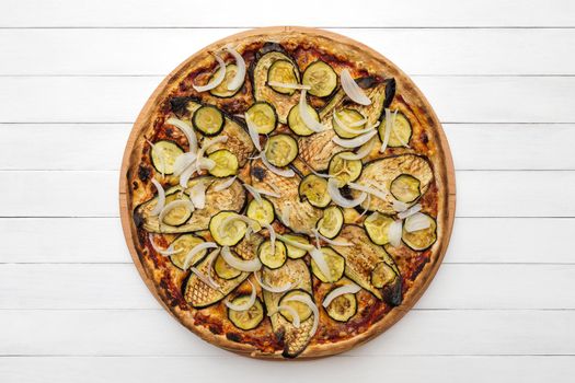 Whole vegetarian pizza topped with grilled eggplant, zucchini and onion, on wooden plate. Top view on white board background. Copy space.