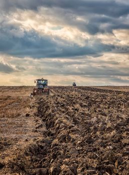 Day view of tractors plowing the soil in a mountain hill.