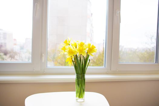 Posy of bright yellow daffodils on white wooden table.