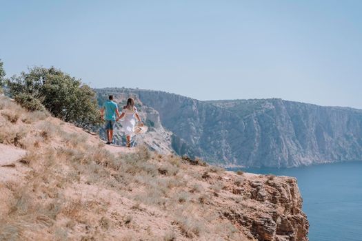 Young woman in a white sundress with a man in light clothes. They walk along the high bank at Cape Fiolent, Crimea. Hold hands and look at the beautiful sea landscape. The concept of romance, travel, adventure.