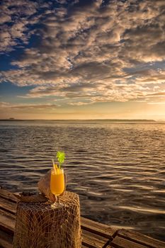 Cocktail with a straw on a wooden table. against the backdrop of the sea sunrise, ocean, at sunset. cocktail in vacation on a tropical island.