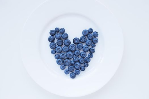 ripe blueberries in a heart shape on a white plate.