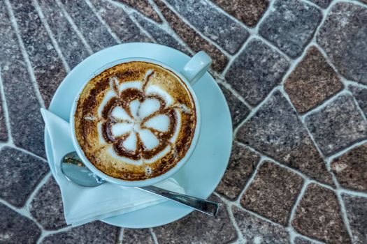 Top view of hot coffee cappuccino latte art in a white ceramic cup with a spoon on a marble table.
