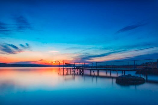 Amazing long exposure sunset on the lake with a bench on the wooden pier.