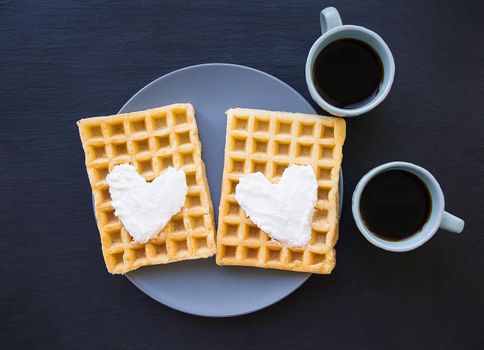 Delicious Belgian waffles with cream on a black background and two cups of coffee