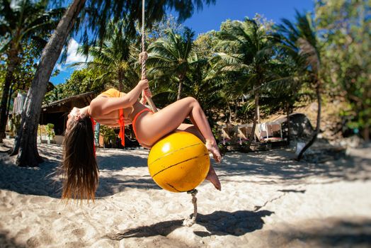 the young girl posing on vacation on the beach on a swing