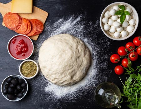 Raw dough for pizza with ingredients and spices on dark black background, top view, flat lay.