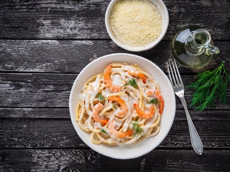 italian pasta spaghetti with shrimps, bechamel sauce and chopped dill on dark rustic wooden table, top view, copy space.