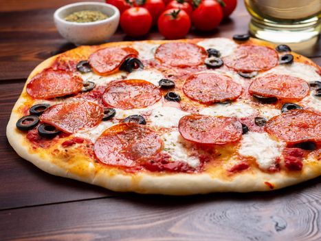 hot homemade Italian pepperoni pizza with salami, mozzarella and olives on a dark brown wooden table.