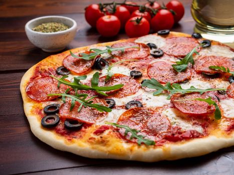 hot homemade Italian pepperoni pizza with salami, mozzarella and olives on a dark brown wooden table.