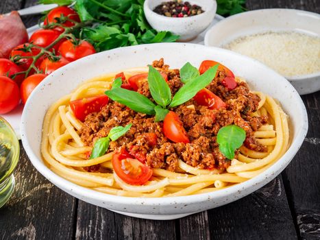pasta bolognese with tomato sauce, ground minced beef, basil leaves on dark rustic wooden table, side view, close-up