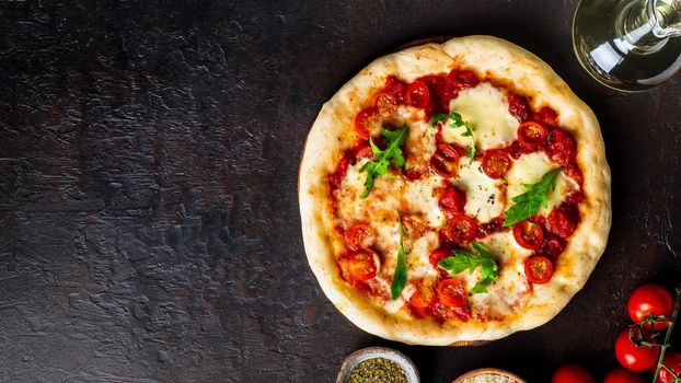 hot homemade Italian pizza margherita with mozzarella and tomatoes on dark brown stone table, top view, copy space.