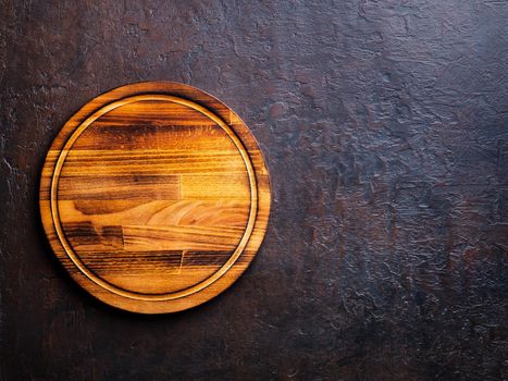 Empty round dark brown wood cutting Board on dark brown stone background, top view, copy space.