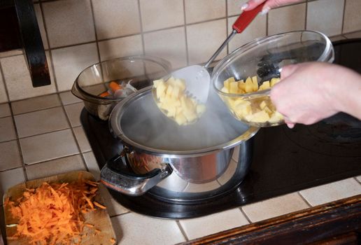 a woman puts potatoes in a pot in the kitchen against the background of fresh vegetables, ingredients for step by step cooking soup. High quality photo