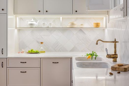 Stylish kitchen with accessories. Bright beige interior with lighted shelves and fresh vegetables on table top. Decorated in vintage style