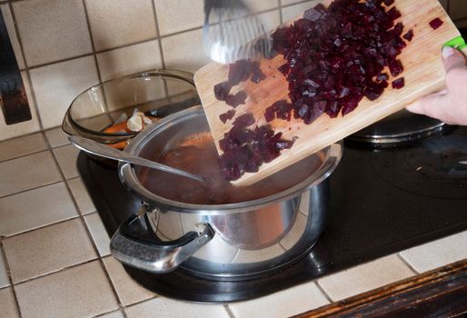 a woman puts a beetroot in a pot in the kitchen against the background of fresh vegetables, ingredients for step by step cooking soup. High quality photo