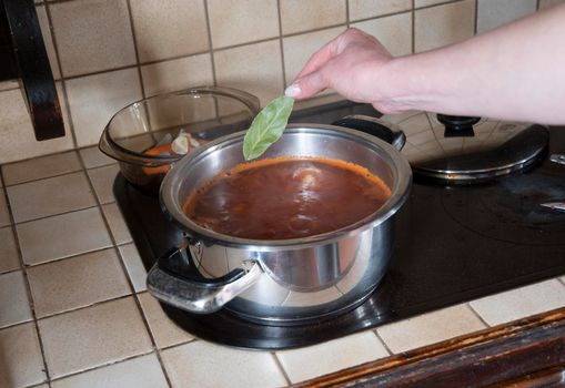 a woman puts a bay leaf in a saucepan in the kitchen against the background of fresh vegetables, ingredients for step by step cooking soup. High quality photo