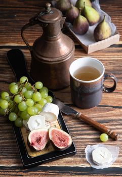 cheese plate with goat cheese, grapes and figs, copper teapot, angle view, healthy food, high-calorie breakfast. High quality photo