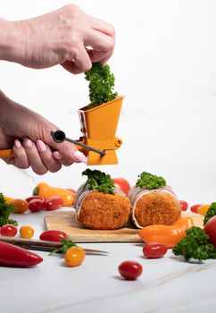 female hands sprinkle ground parsley on minced meat sausages in bacon with green parsley and fresh vegetables, cherry tomatoes, bell peppers, colorful food . High quality photo