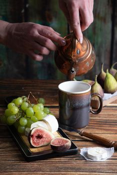 cheese plate with goat cheese, grapes and figs, copper teapot, angle view, healthy food, high-calorie breakfast. High quality photo