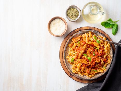 fusilli pasta with tomato sauce, chicken fillet with basil leaves on light white wooden background, top view, copy space.