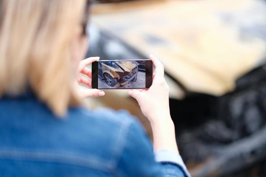 Woman insurance broker making photo of burnt car. Automobile accident and insurance case concept