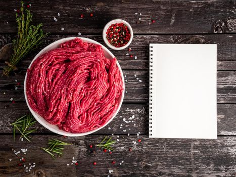 Mince beef, ground meat with ingredients for cooking on old gray dark wooden rustic table, notepad, recipe mock-up, top view, copy space.
