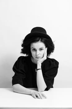 A woman in a hat sits at a table, white background. High quality photo