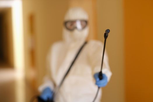 Person in protective suit holding disinfection equipment in hand. Respirator disinfects of apartment with chemical agent, sanitation worker cleans room from coronavirus