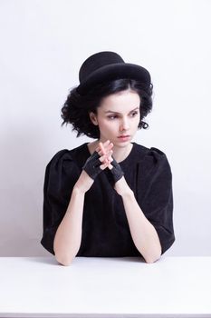 A woman in a hat and fingerless gloves sits at a table. High quality photo