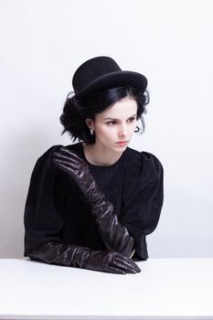 a woman in a hat and long gloves sits at a table. High quality photo