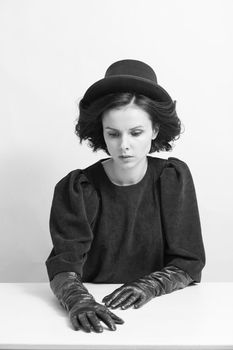 curly woman in a hat and gloves sits at a white table, black and white photo. High quality photo