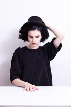 A woman in a hat sits at a table, white background. High quality photo