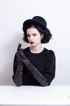 a woman with red lips, curly hair in a black hat and gloves sits at a table. High quality photo