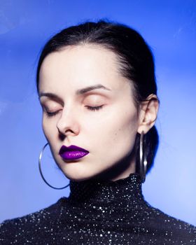woman with closed eyes in a black turtleneck with sequins on a blue background. High quality photo