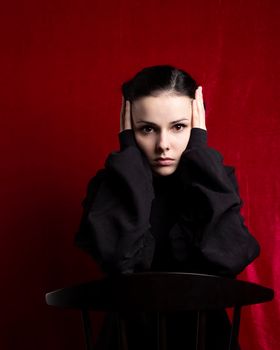 a woman in a black sweater sits at a chair, red background. High quality photo